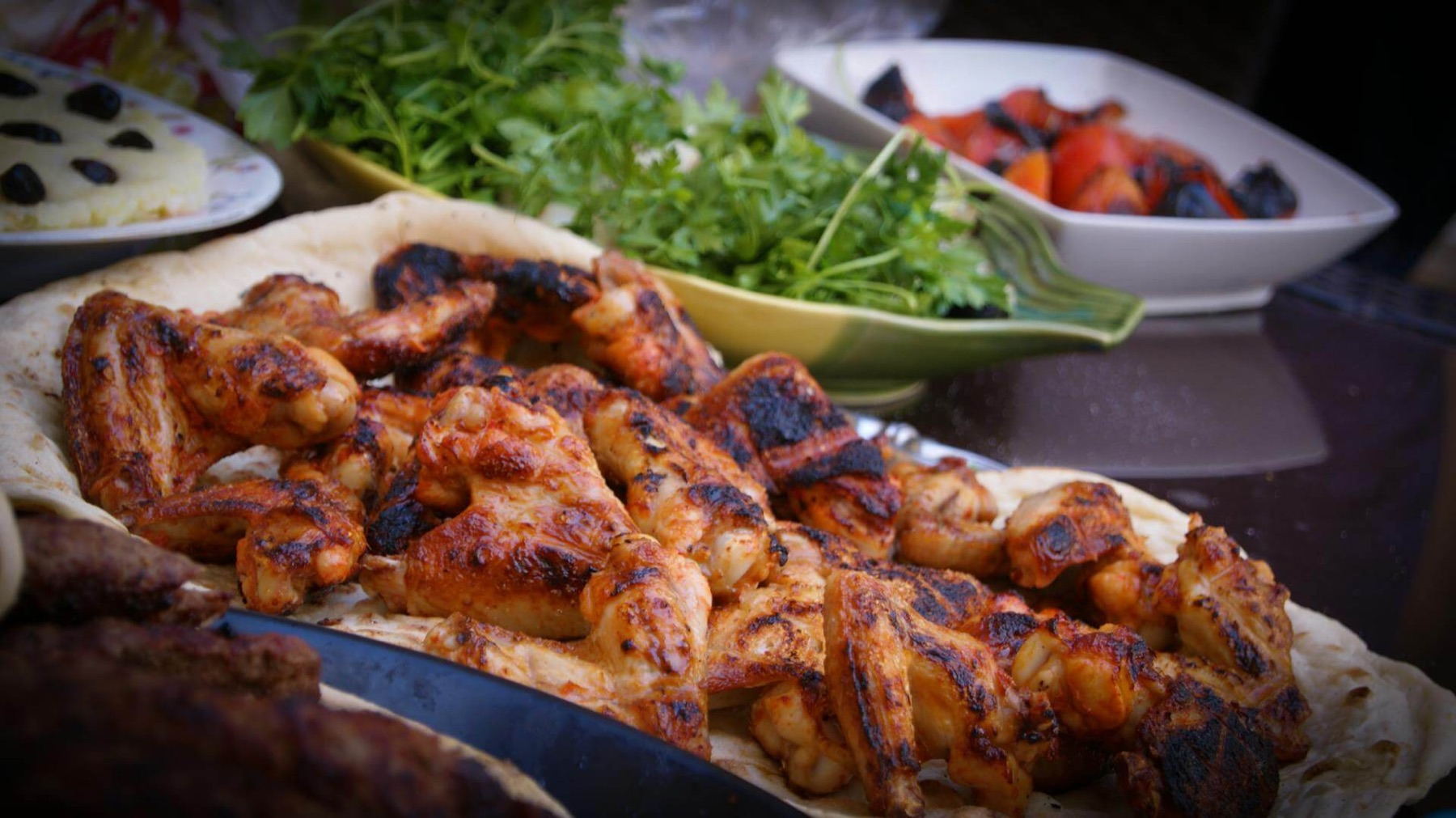 Grillade kycklingbitar med grillstrimmor på tunnbröd, bredvid en skål med färsk persilja och ett fat med grillad paprika