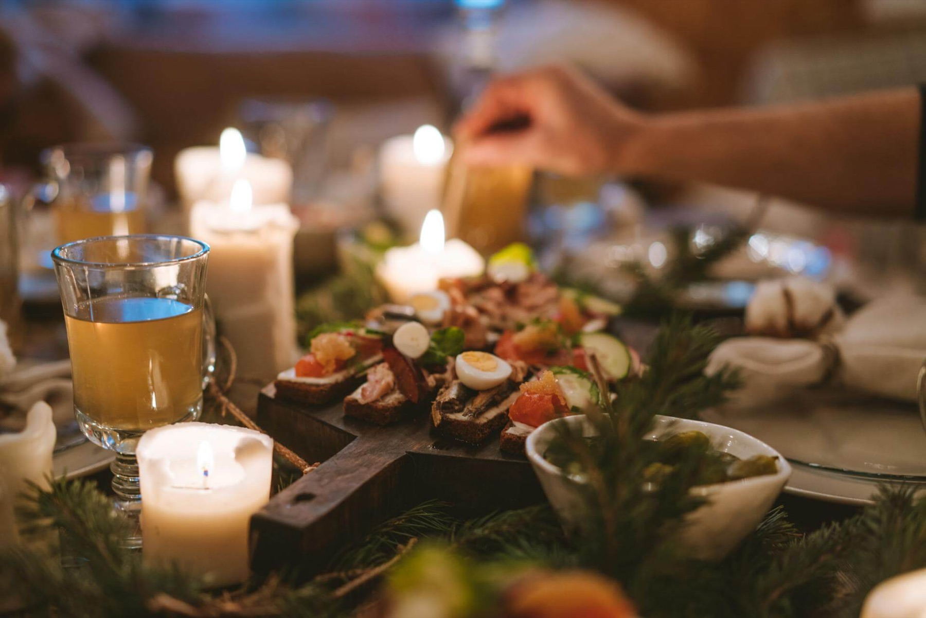 Julbord i levande ljus med snittar på en stjärnformad träbricka, granris och ett glas glögg
