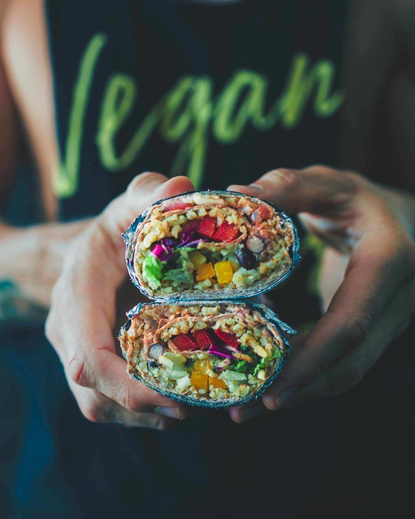 Två händer håller upp en wrap delad i två halvor, fylld med ris, bönor, paprika, rödkål och avokado